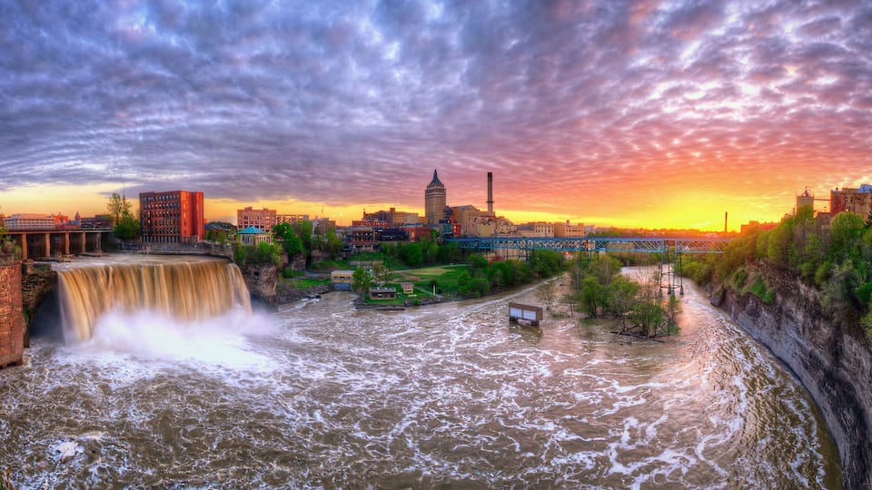 A waterfall, a river, a bridge, and a city skyline at sunset.
