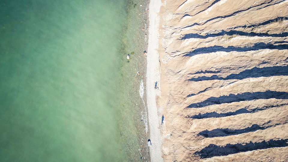 An aerial view of a beach with clear water and layered rock formations.