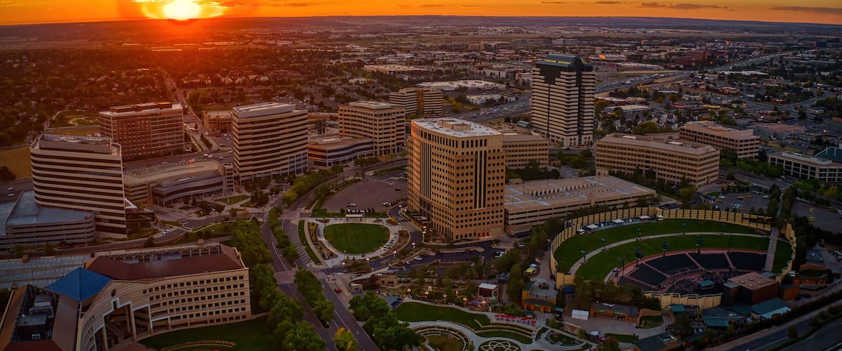 A cityscape at sunset with prominent buildings, a stadium, and a large open field.
