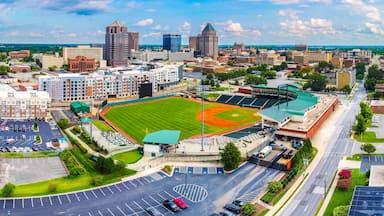 A cityscape with a baseball stadium surrounded by urban buildings and a parking lot.