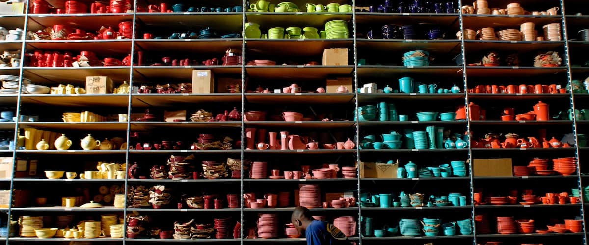 A warehouse with shelves stocked with various colored ceramic dishes and pots.