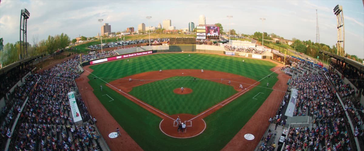 A baseball stadium with a large crowd, a baseball diamond, and city buildings in the background.