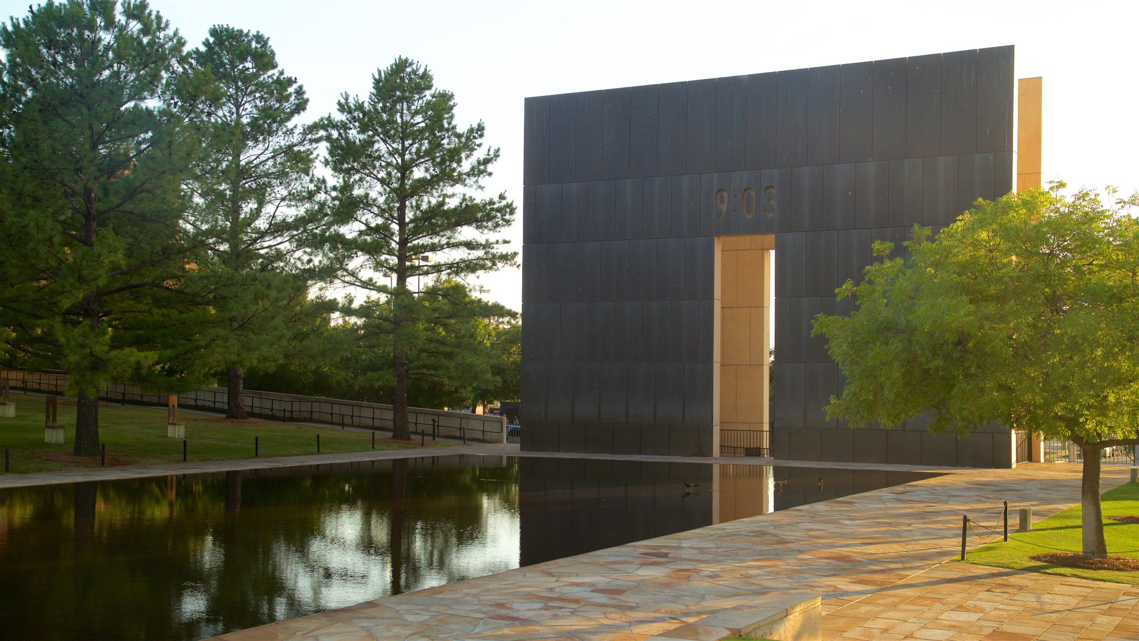 A modern building with a large digital clock displaying 9:03, surrounded by a reflective water body and trees.
