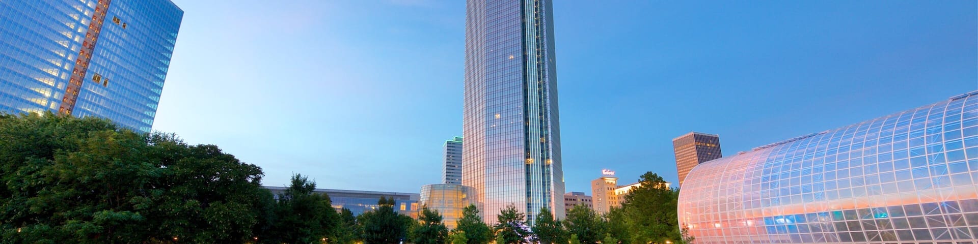A modern cityscape with a prominent skyscraper, a glass dome structure, and a river.