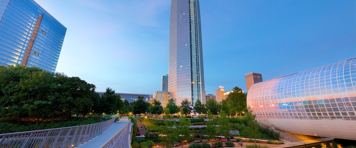 A modern cityscape with a prominent skyscraper, a glass dome structure, and a river.