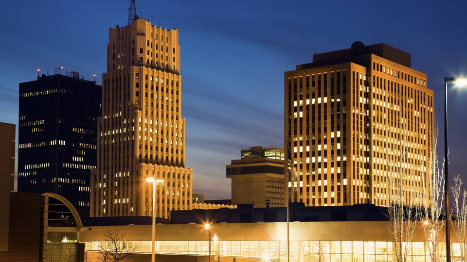 A cityscape at dusk with illuminated buildings and a clear sky.