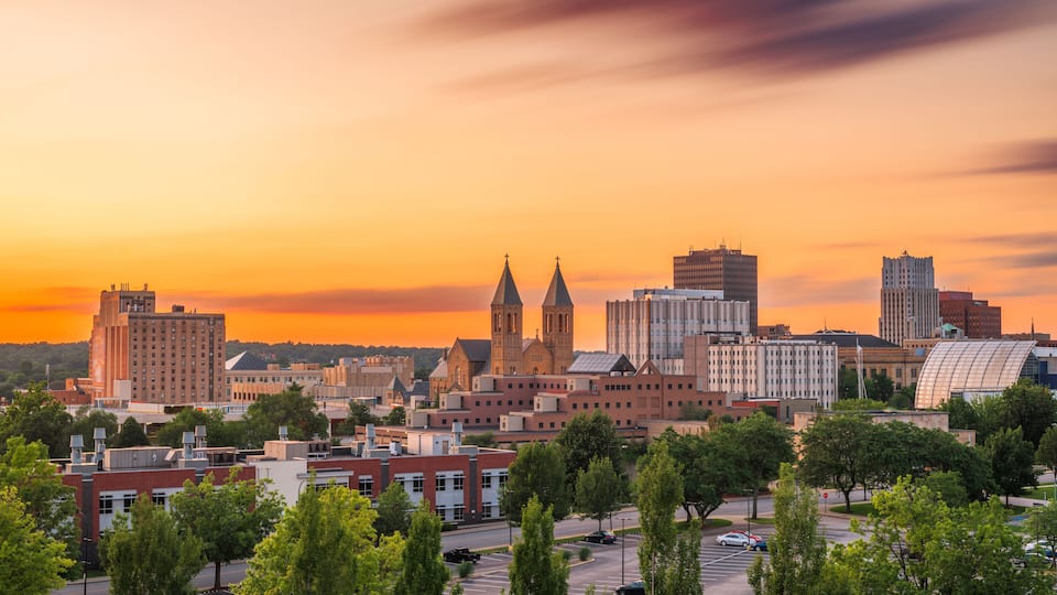 A cityscape with a prominent church with twin towers, surrounded by modern buildings and a sunset sky.