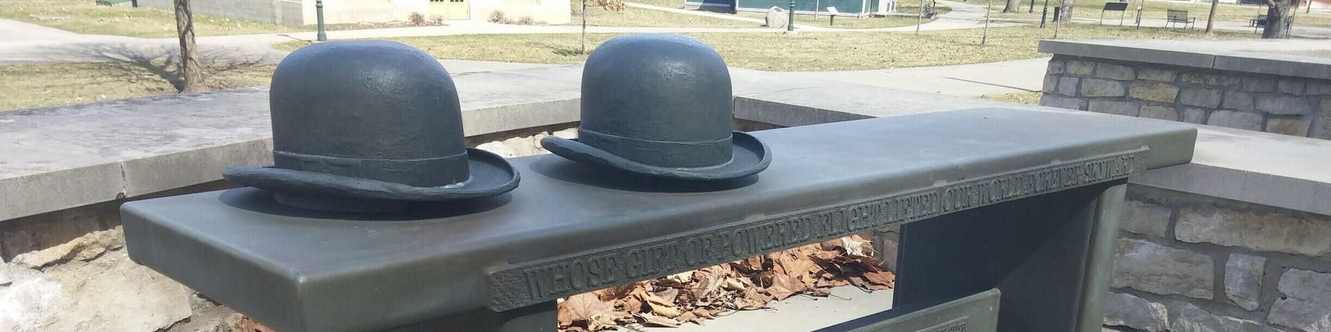 A bench with two black hats on top, surrounded by a stone wall and a grassy area.