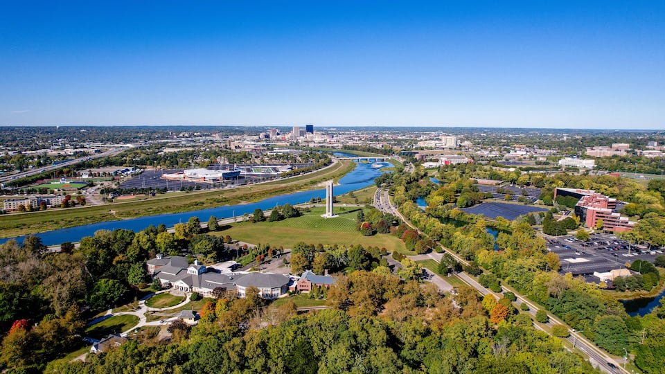 A river flowing through a city with a tall monument, green parks, and various buildings.