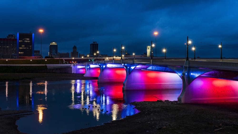 A bridge with colorful lights reflecting on the water.