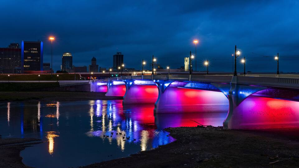 A bridge with colorful lights reflecting on the water.