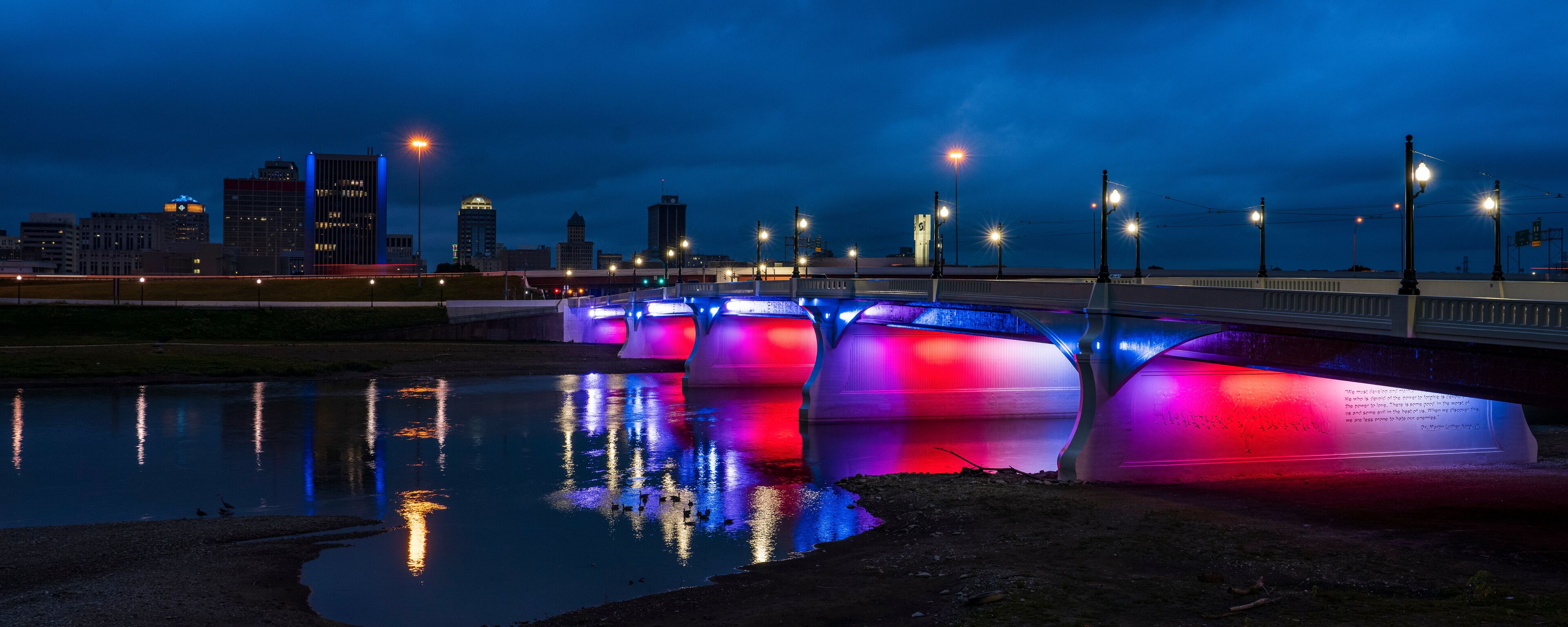 A bridge with colorful lights reflecting on the water.