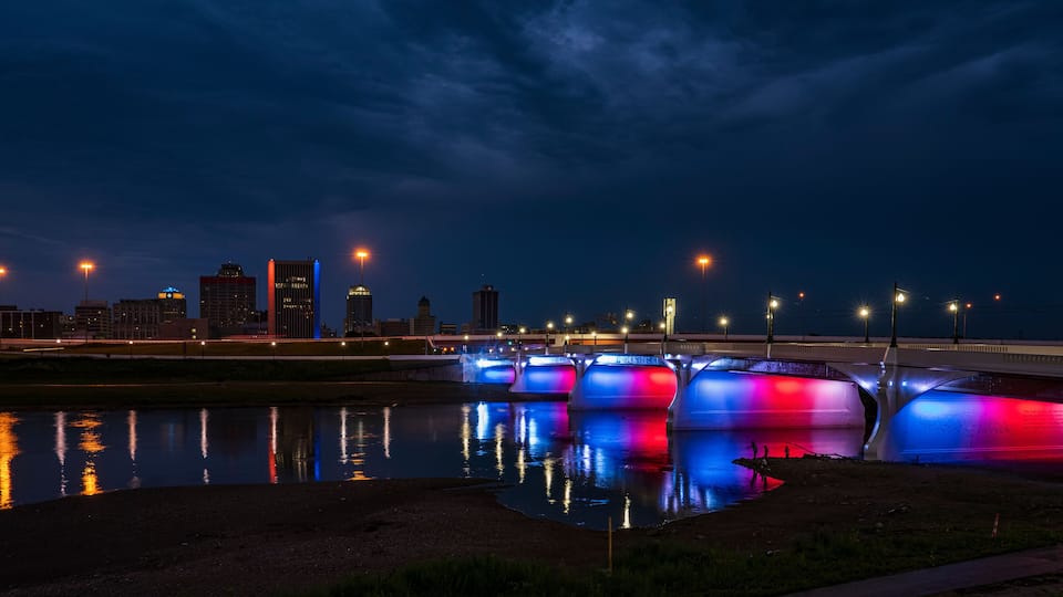 A nighttime cityscape with illuminated bridges reflecting on a calm river.