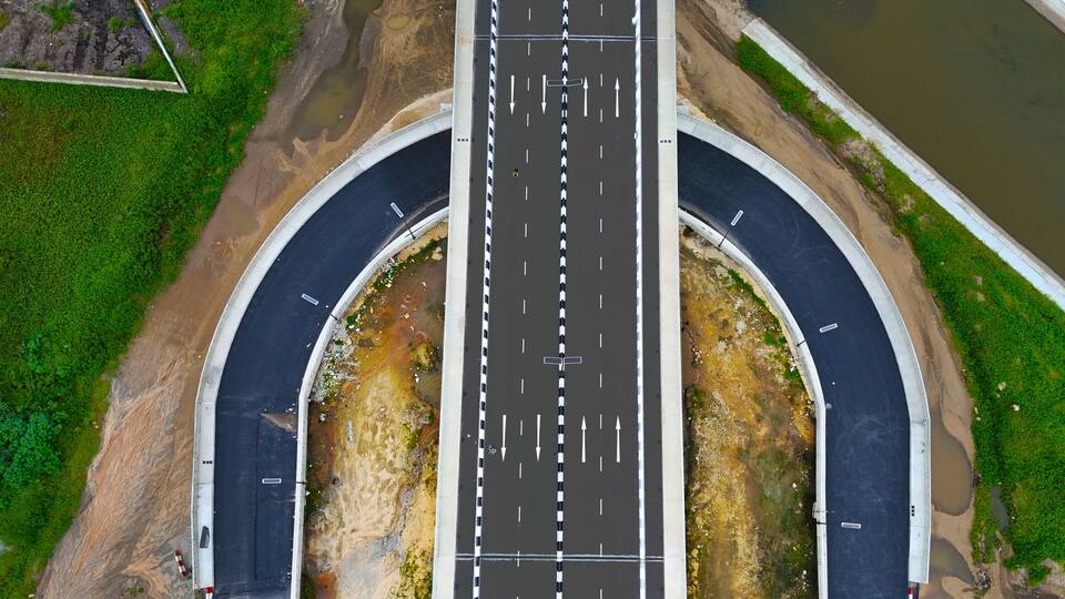Aerial view of a sleek, modern highway interchange with sharp black asphalt contrasting with surrounding green vegetation, Ikeja, Lagos, Nigeria.