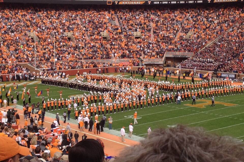 A football stadium filled with spectators, a marching band, and a football field.