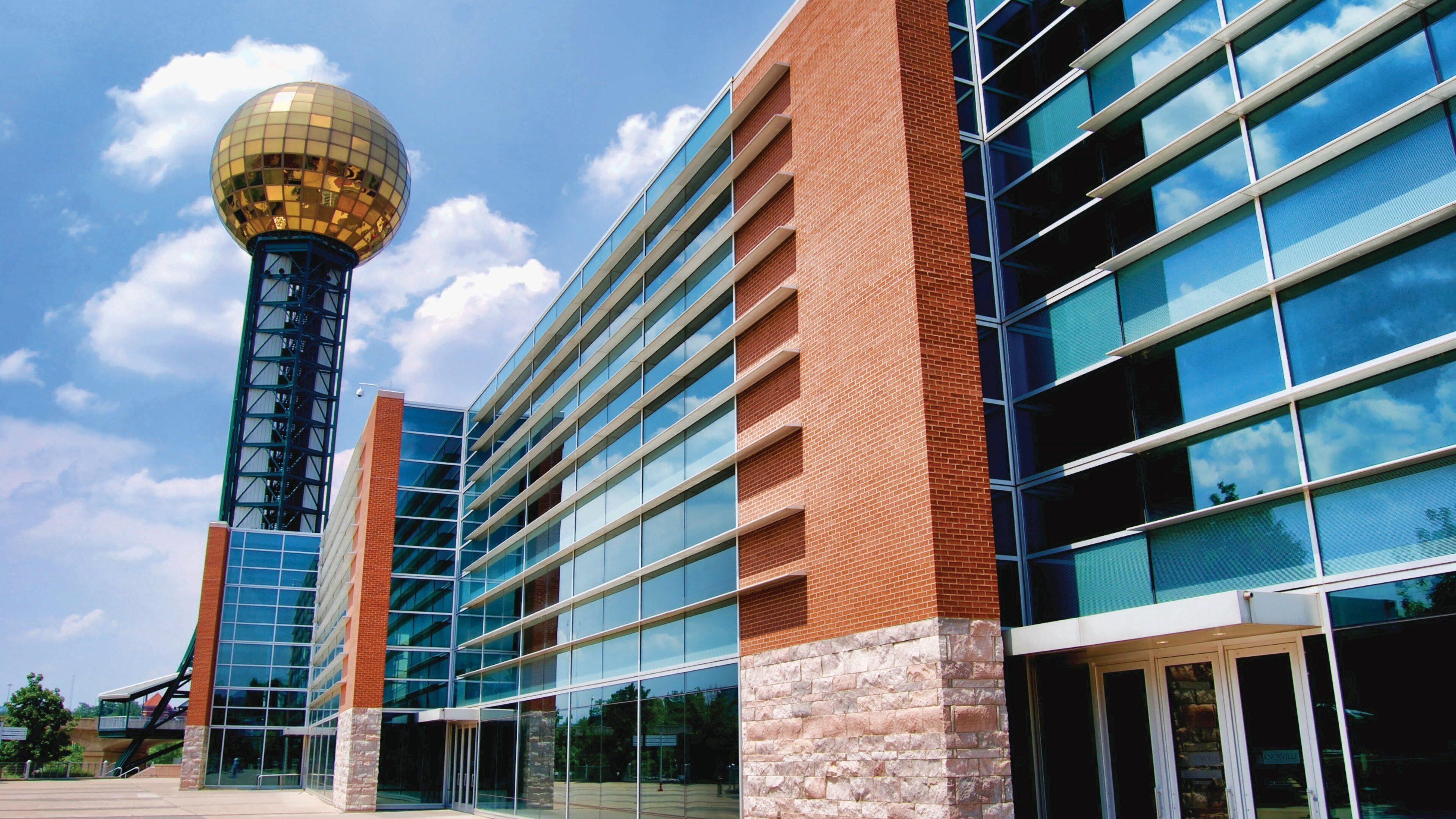 A modern building with a glass facade and a brick base, a spherical structure on a tower, and a clear blue sky.
