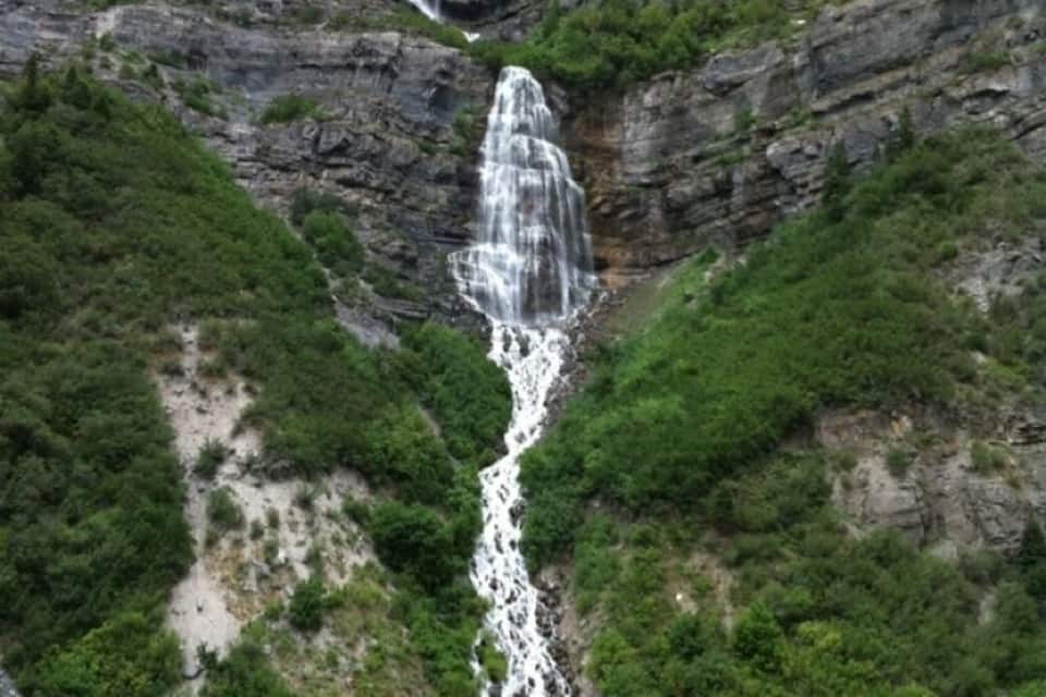 A multi-tiered waterfall cascading down a rocky cliff surrounded by dense greenery.