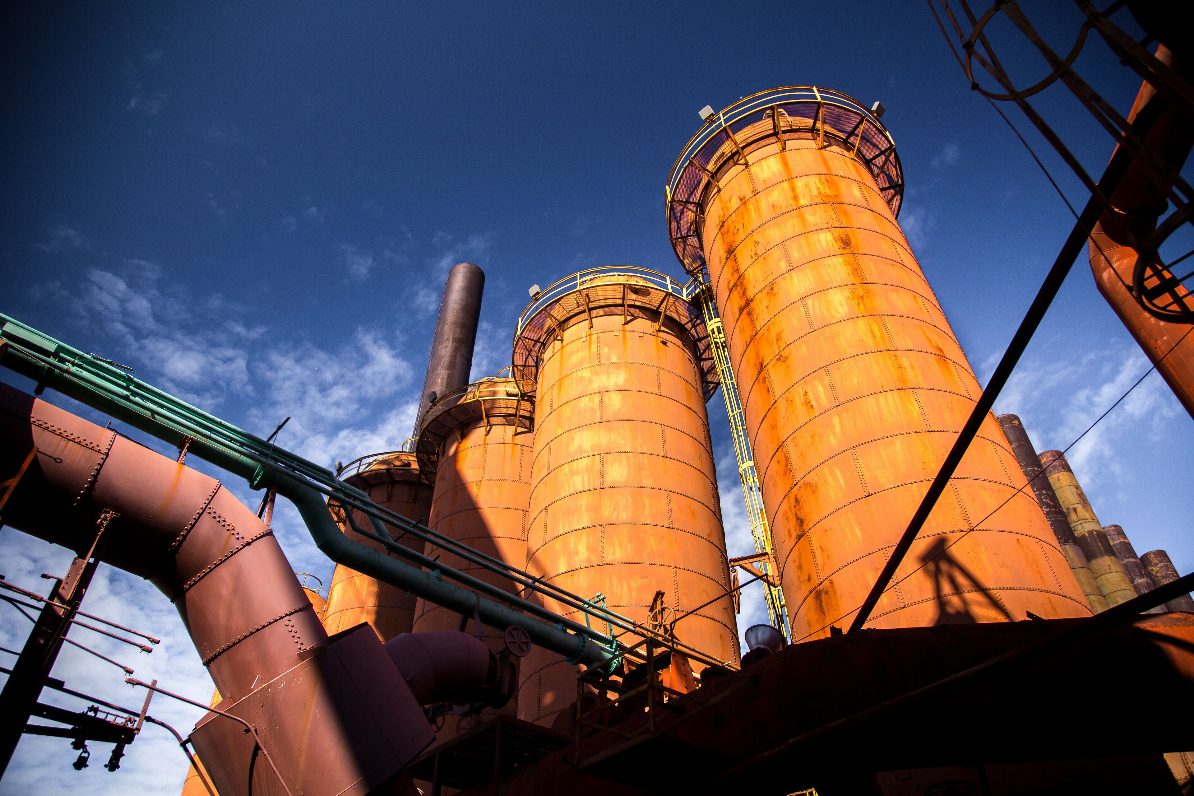 Industrial silos and pipes against a clear blue sky.