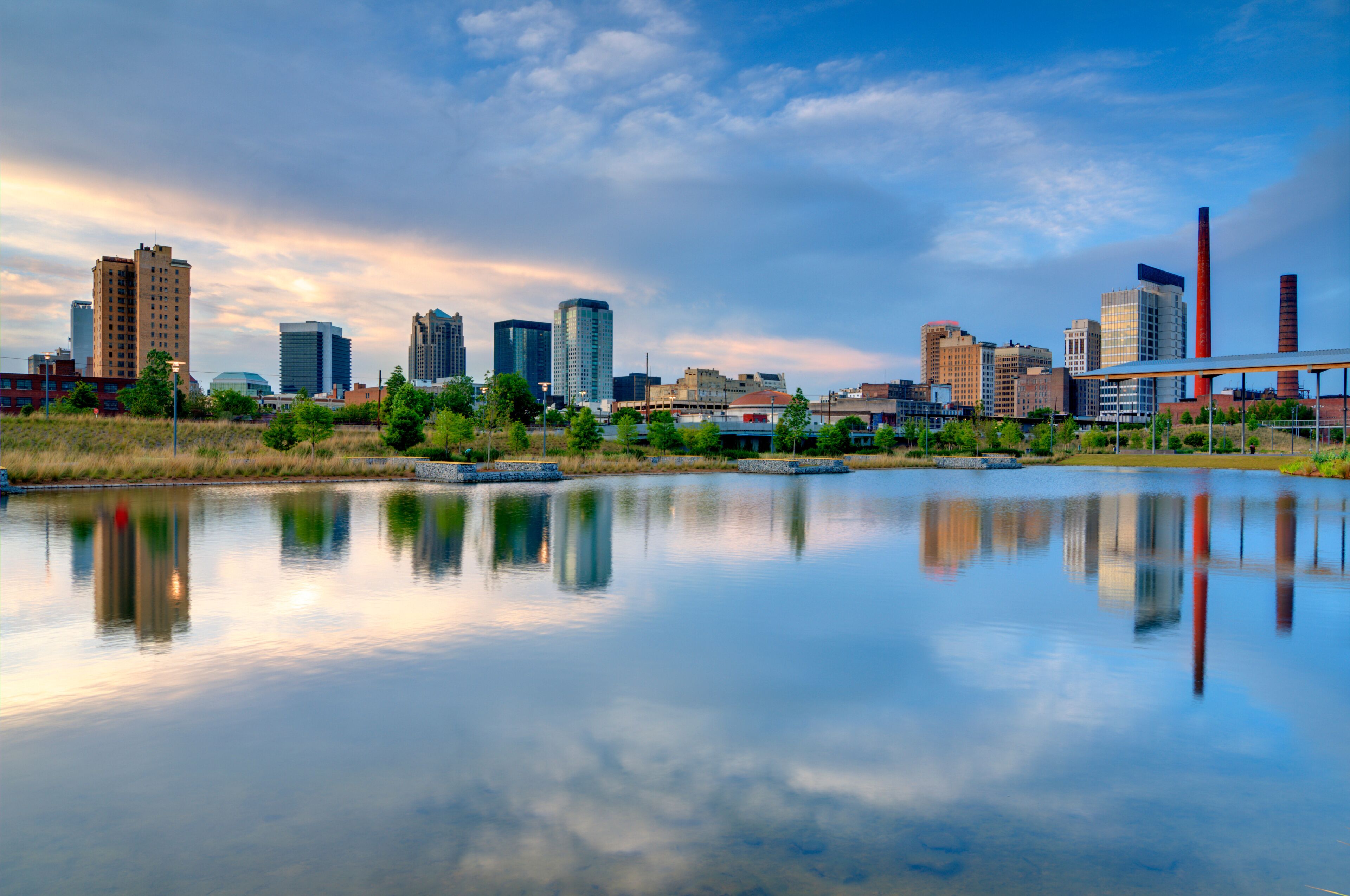 A city skyline with modern buildings, a river reflecting the structures, and a bridge in the distance.