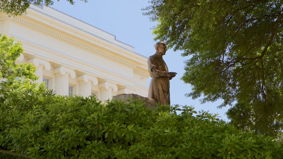 A statue of a man standing on a rock with a building in the background.