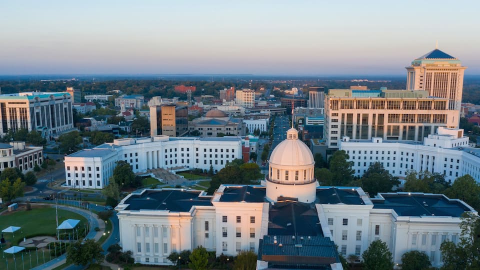 A cityscape with a prominent white building with a dome and a tall tower with a pointed roof.