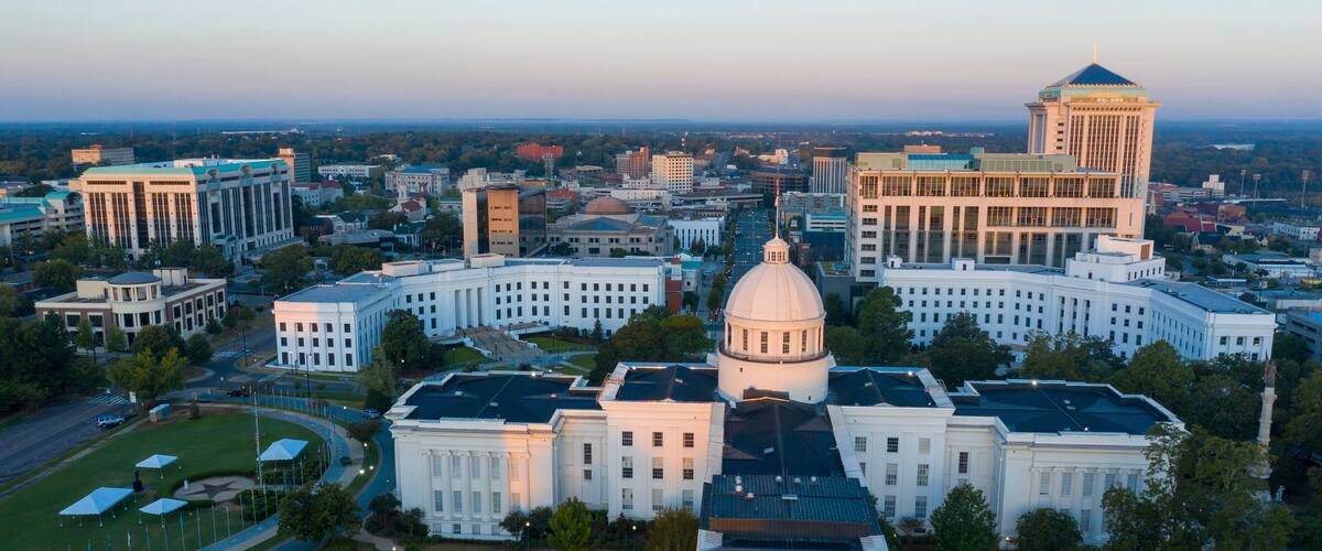 A cityscape with a prominent white building with a dome and a tall tower with a pointed roof.