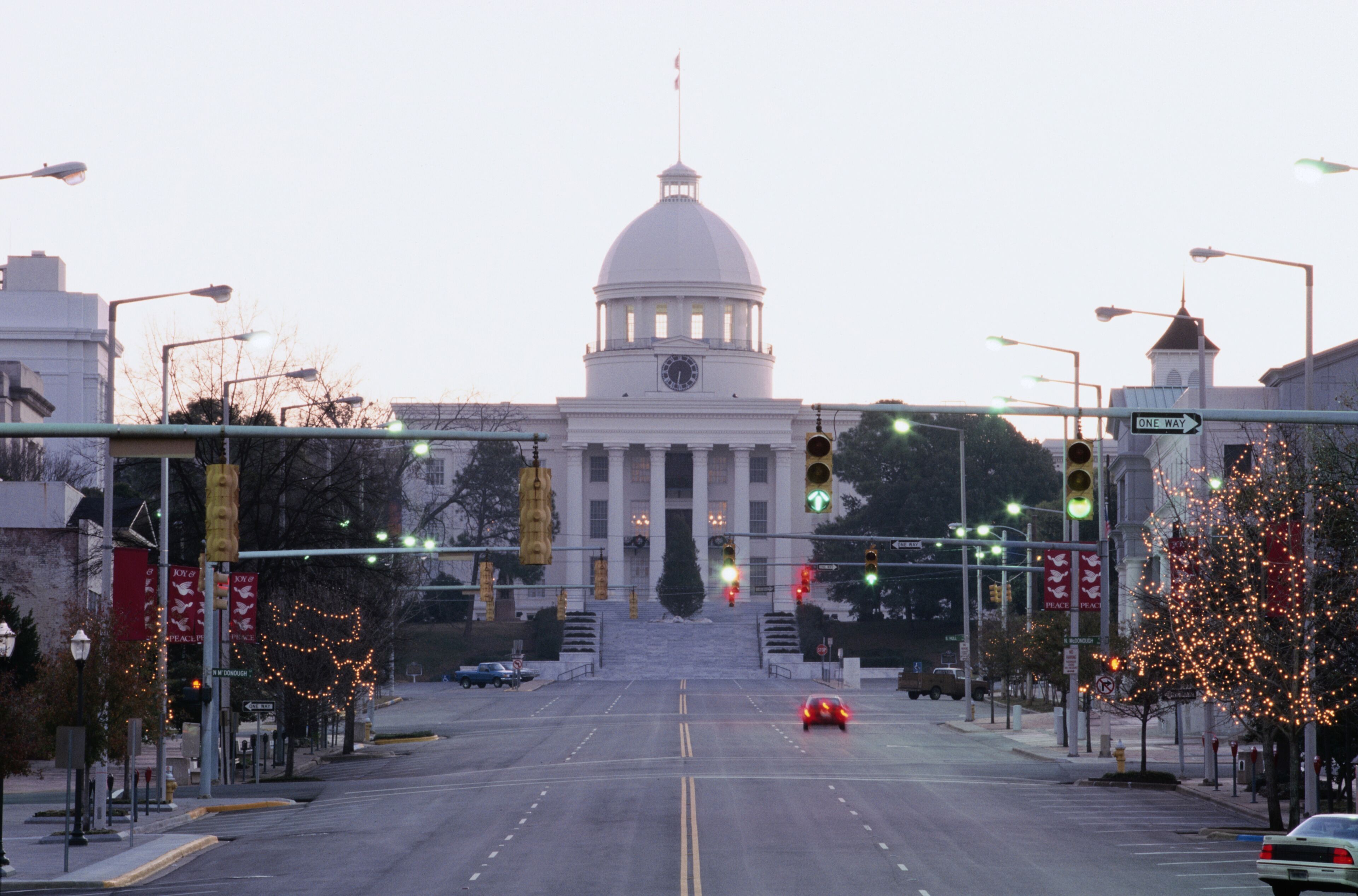 A city intersection with traffic lights, a one-way sign, and a large building with a dome and clock.