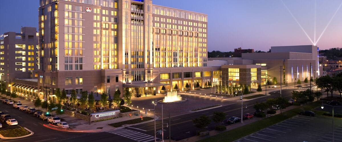 A large, well-lit hotel with a distinctive blue-lit tower, surrounded by a parking lot and a fountain.