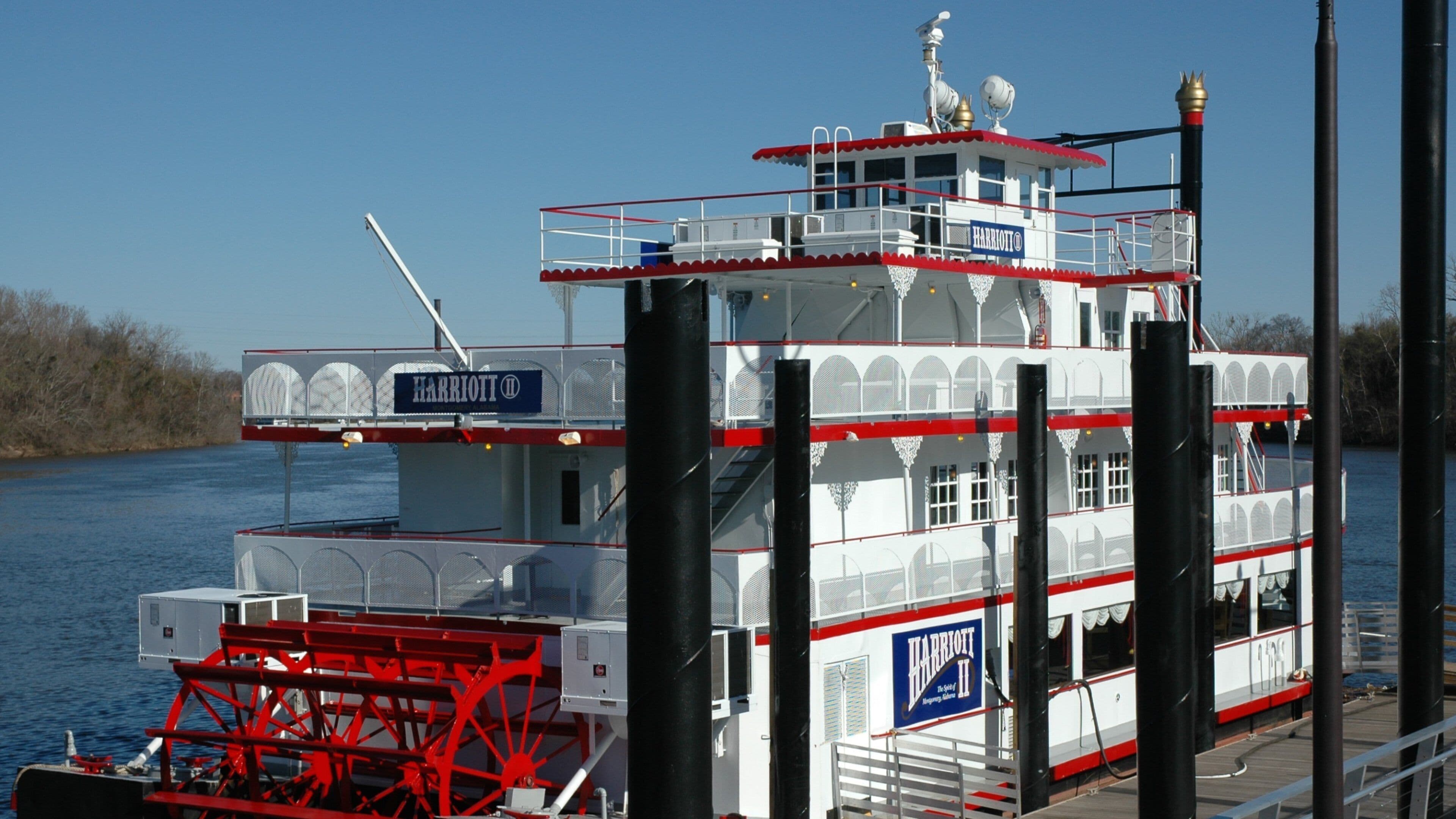 A large white and red ferry with 'Harriott' branding, docked at a pier with a clear blue sky in the background.