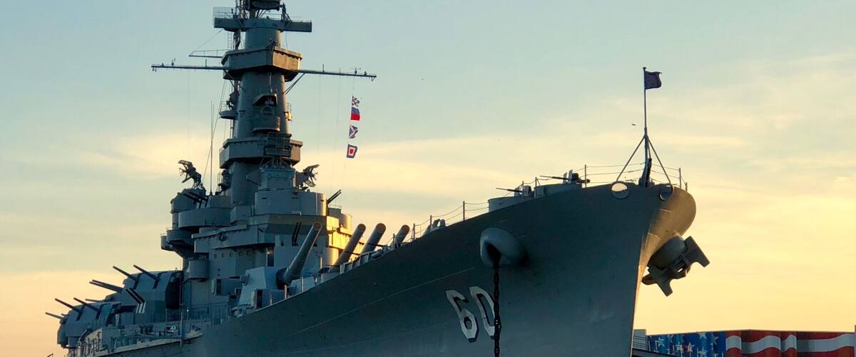 A large naval ship docked at a port with a clear sky in the background.