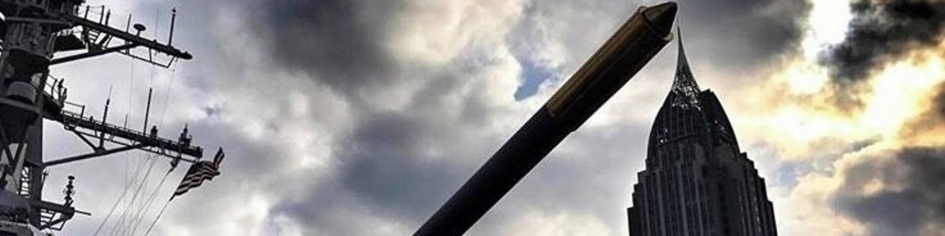 Un buque de guerra con un cañón grande, un rascacielos alto y un cielo nublado.