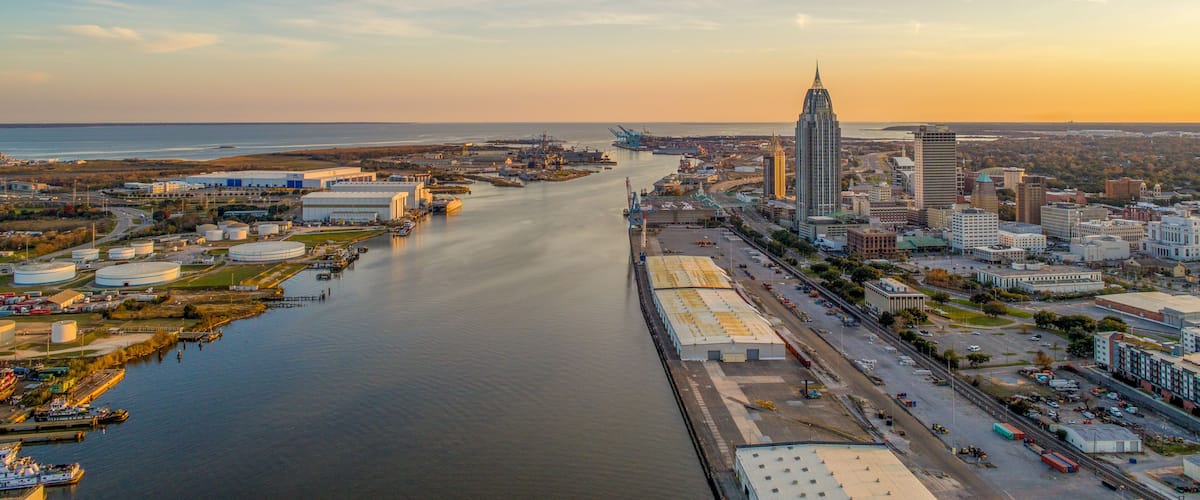 A river flowing through a city with industrial buildings, a tall skyscraper, and a bridge.