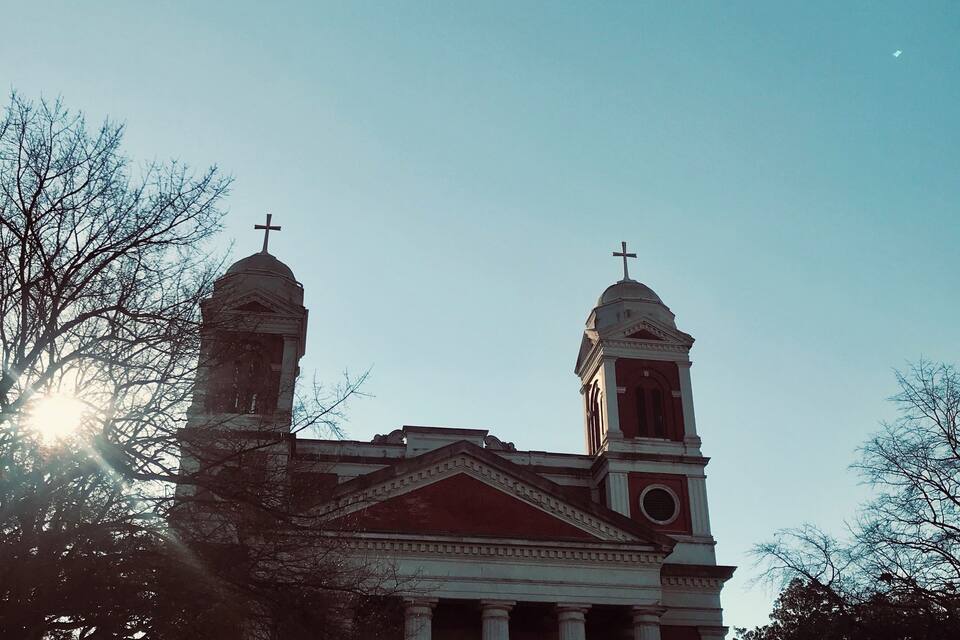 A church with two towers and a clock tower, surrounded by trees.