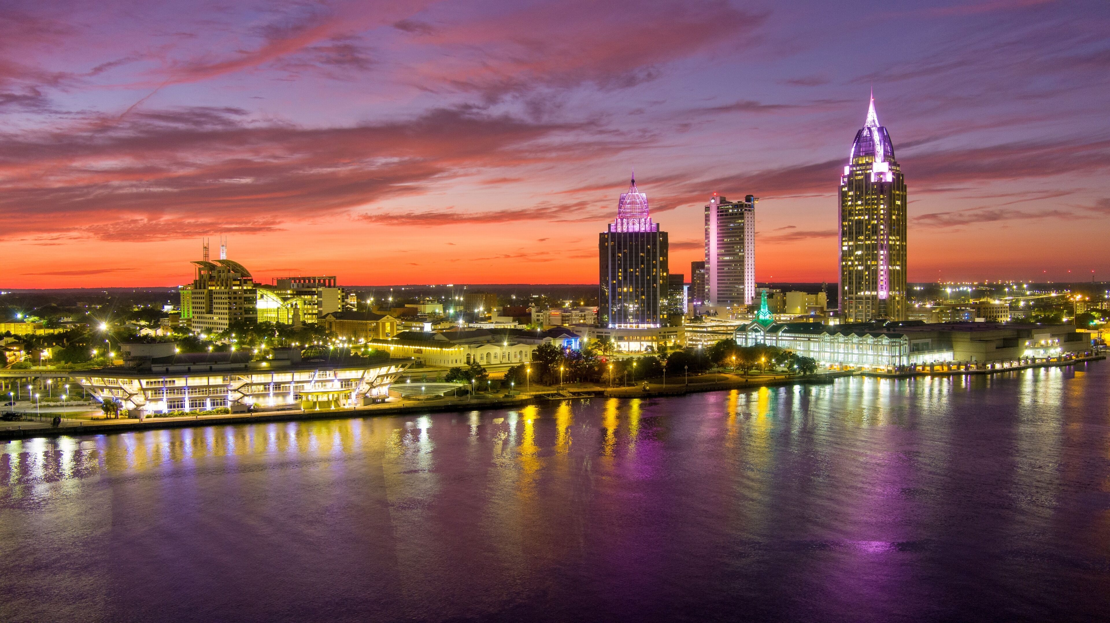 A city skyline at dusk with illuminated buildings reflecting on the water.
