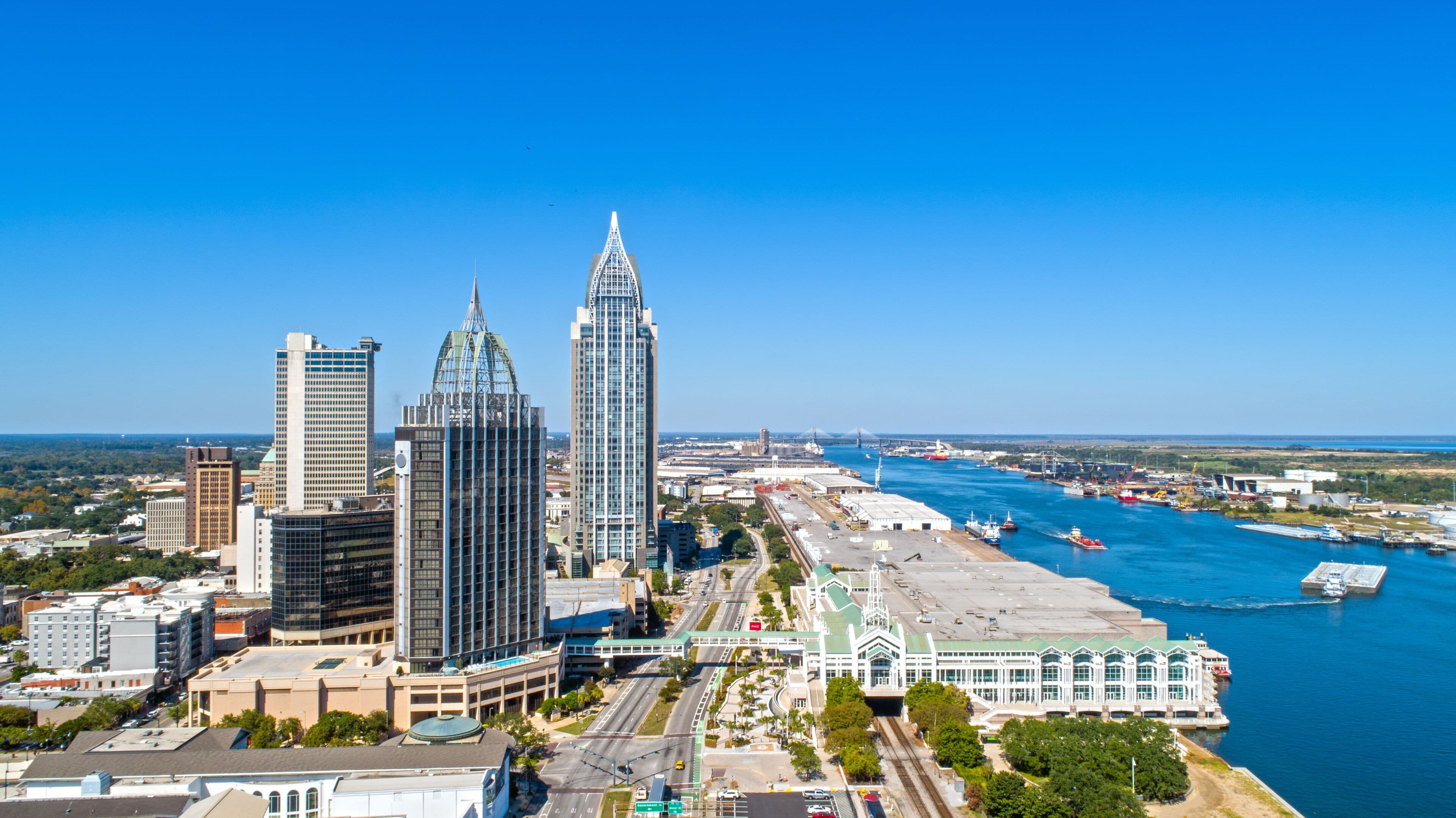 A city skyline with prominent skyscrapers, a river with boats, and a bridge in the distance.