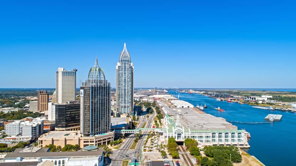 A city skyline with prominent skyscrapers, a river with boats, and a bridge in the distance.
