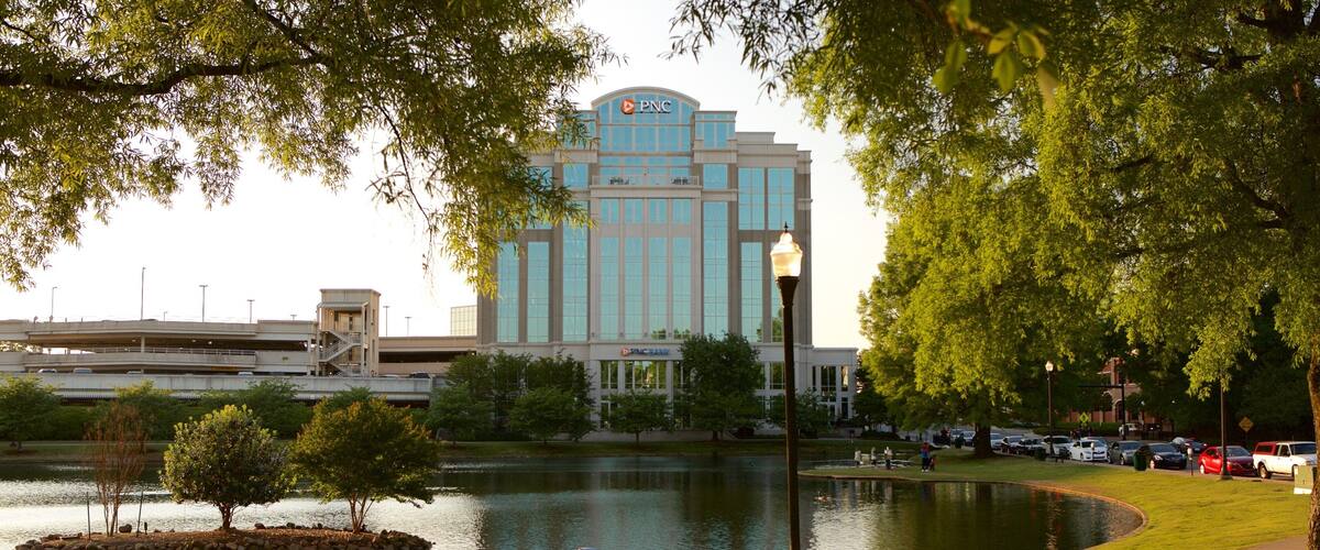 A lake with ducks, a bench, and a large building with 'PNC' on it.