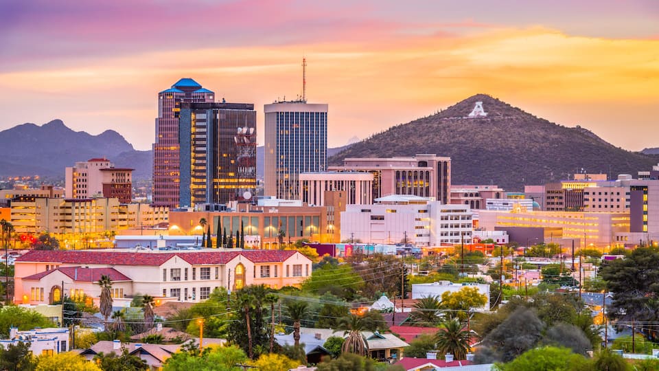 A cityscape with modern buildings, a mountain, and a sunset sky.