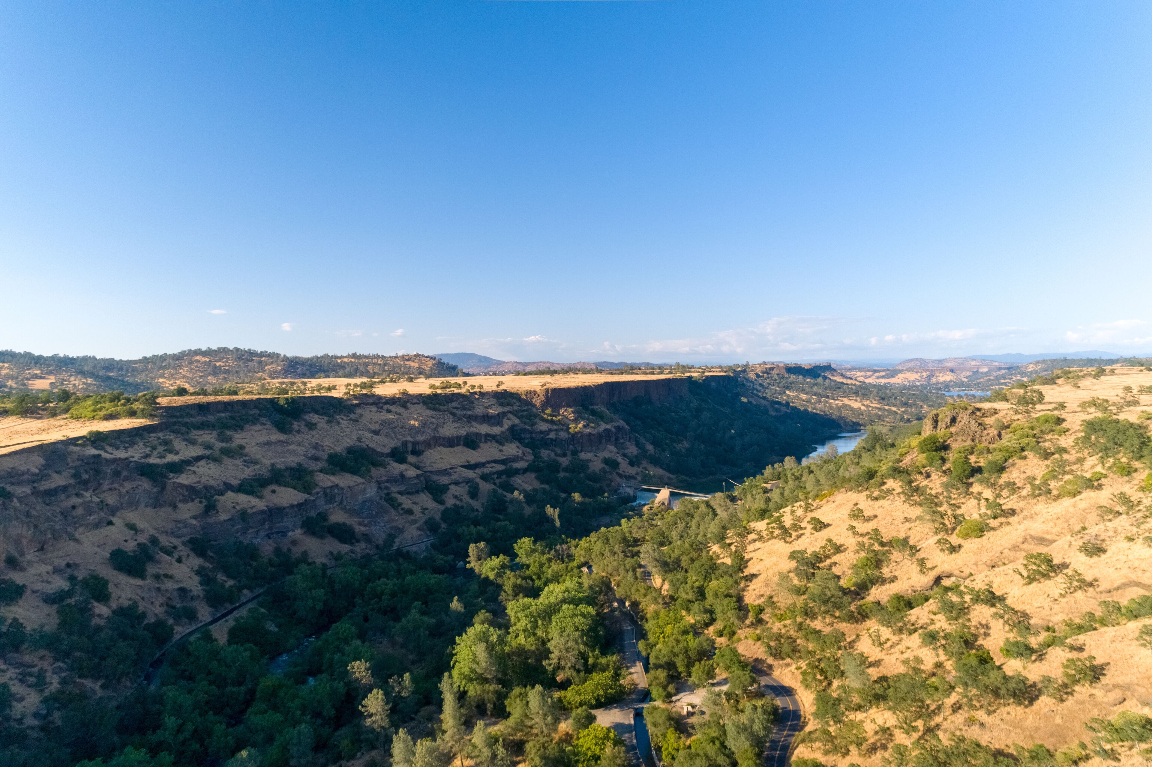 A canyon with a river, surrounded by hills and sparse vegetation.