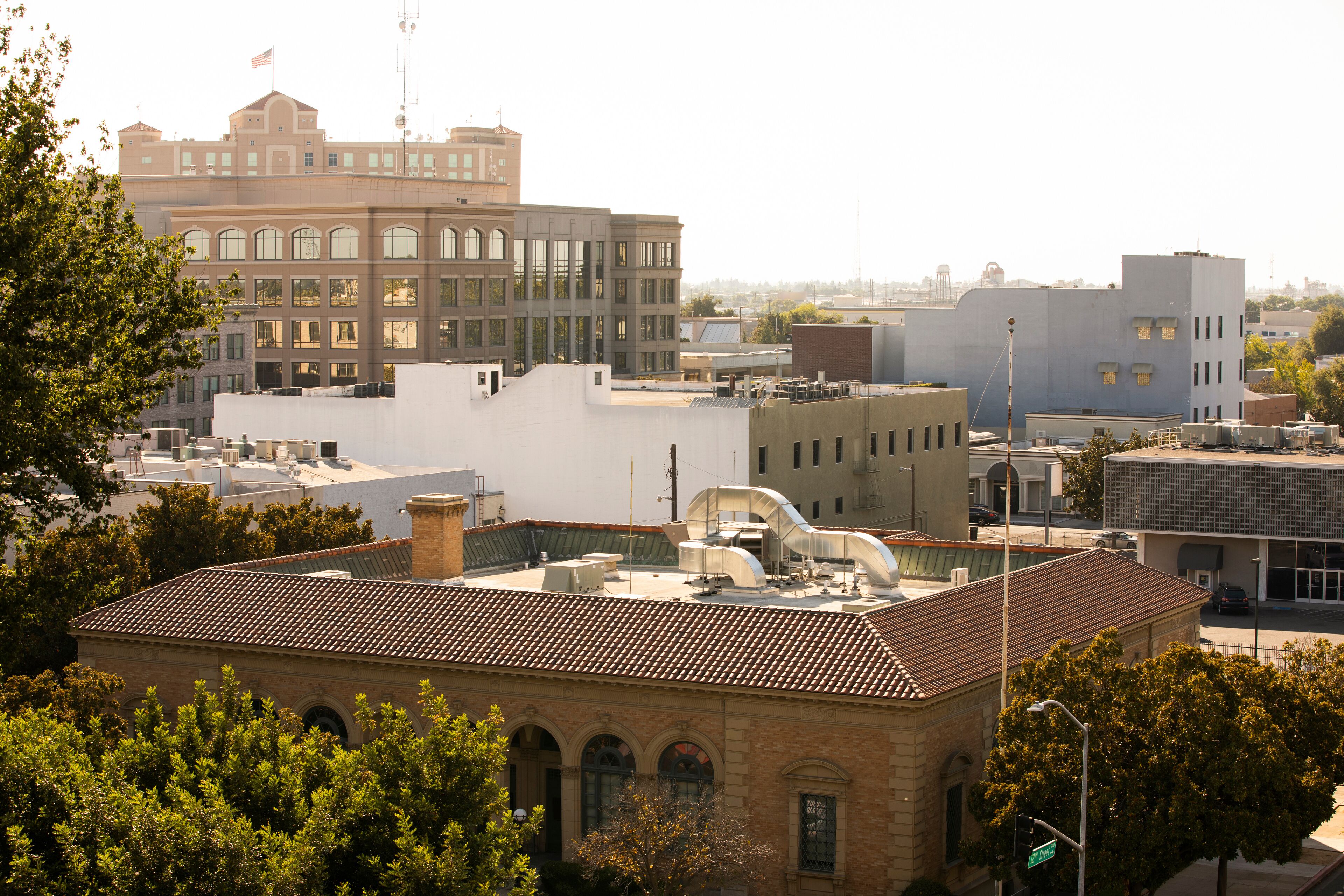 A cityscape with a mix of historical and modern buildings, a prominent flag on a tall building, and a clear sky.