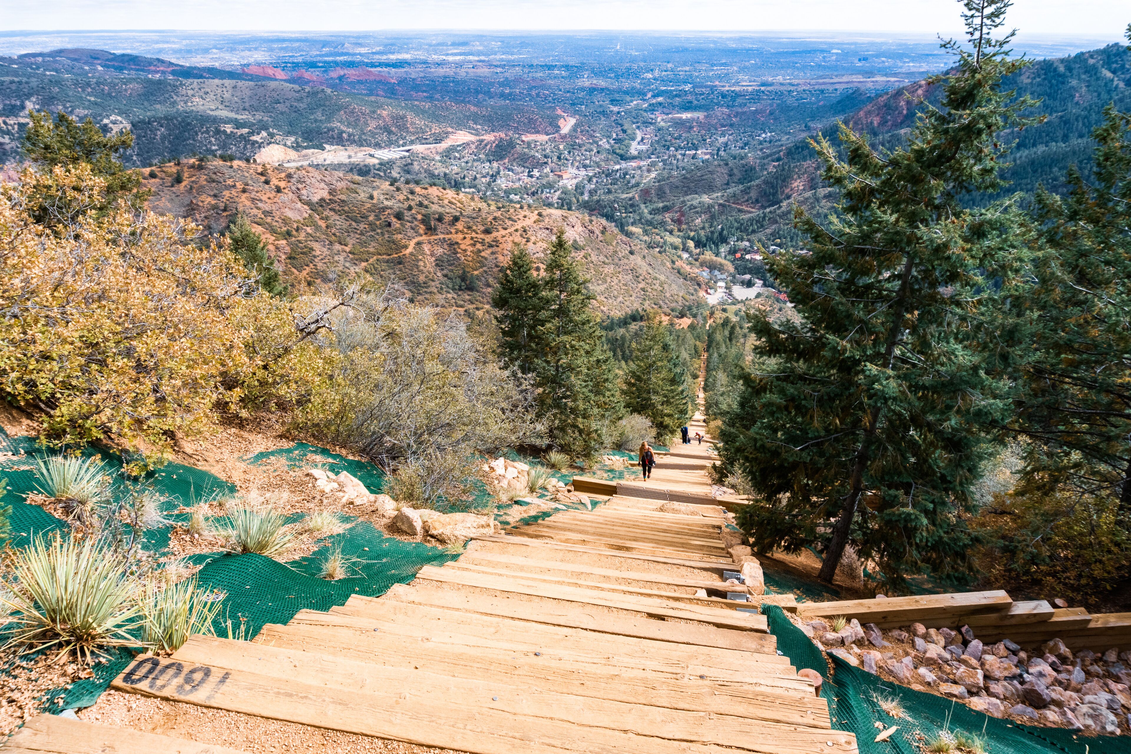 A wooden staircase leading down a hillside with a view of a valley and distant city.