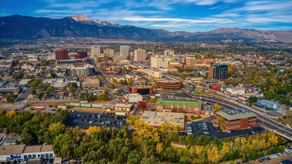 A cityscape with mountains in the background, a mix of modern and historic buildings, and a parking lot.