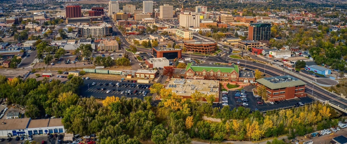 A cityscape with mountains in the background, a mix of modern and historic buildings, and a parking lot.