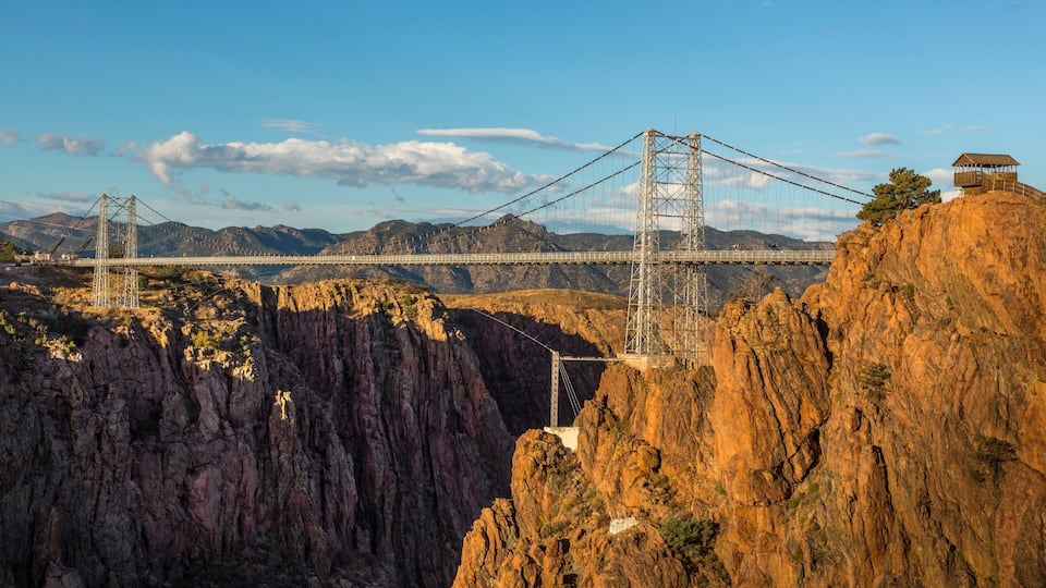 A suspension bridge spanning a deep gorge with rocky cliffs on either side.