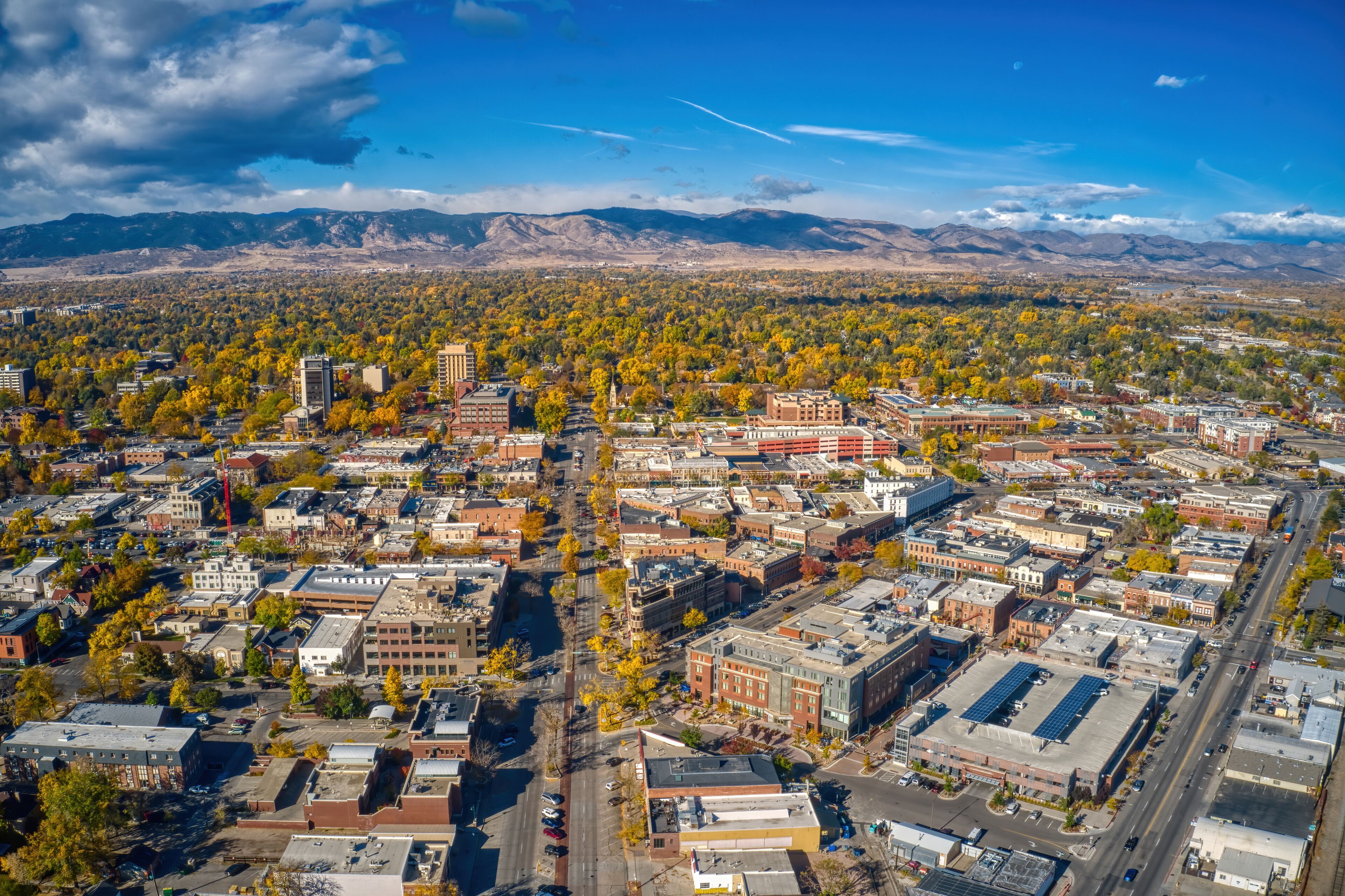 An aerial view of a city with autumn foliage, a river, and mountains in the background.