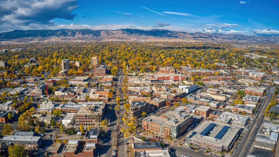 An aerial view of a city with a river running through it, surrounded by mountains and autumn foliage.