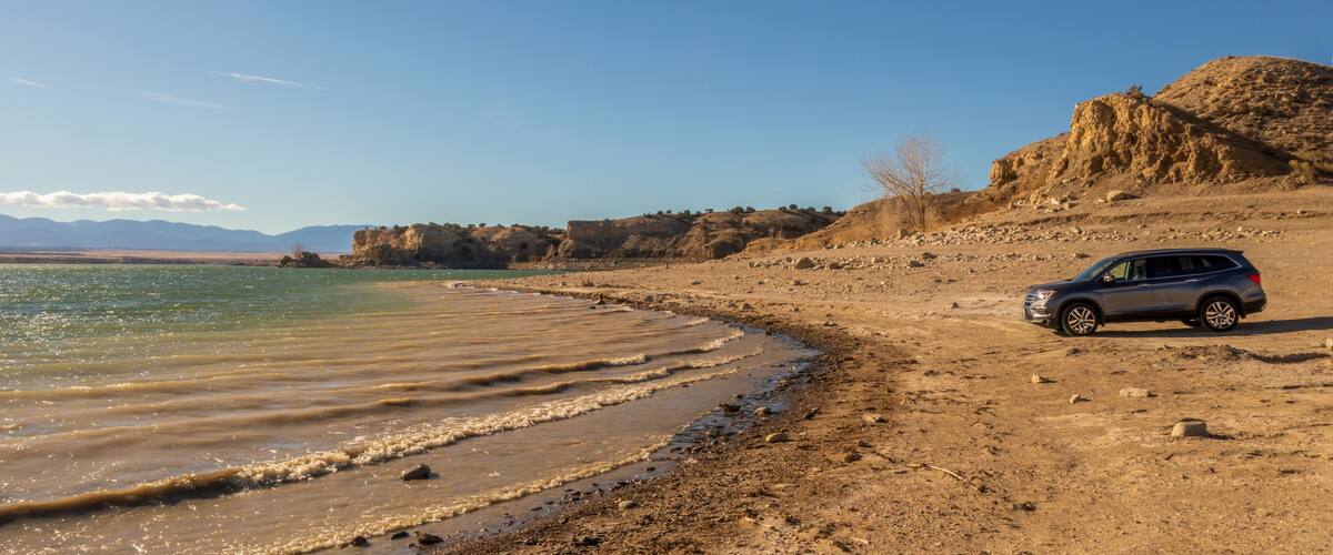 A beach with a car parked on the sand, rocky cliffs, and a clear sky.