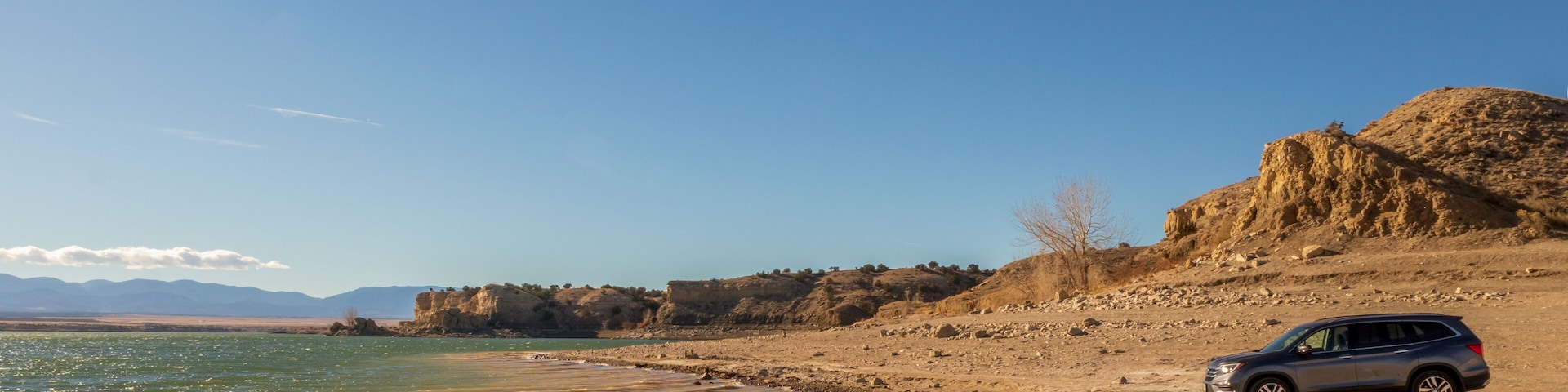 A beach with a car parked on the sand, rocky cliffs, and a clear sky.