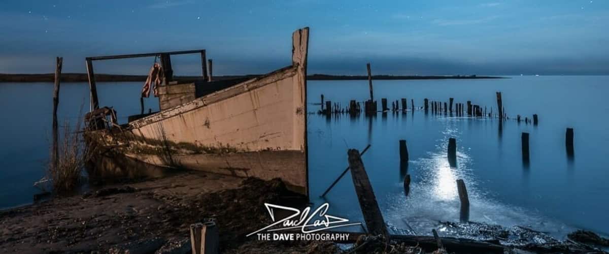 A moonlit night scene with a derelict boat and wooden posts in a calm body of water.