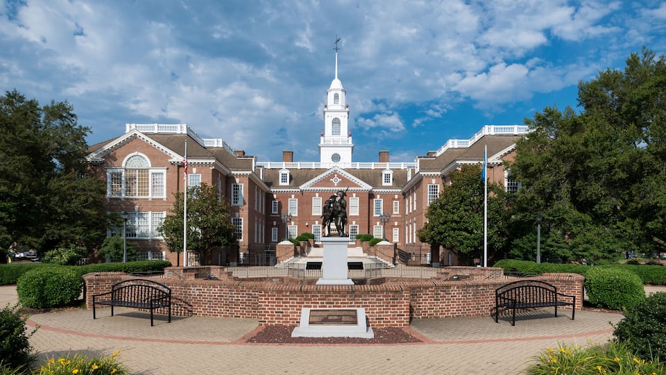 A historic building with a central tower, a statue in front, and a brick walkway.